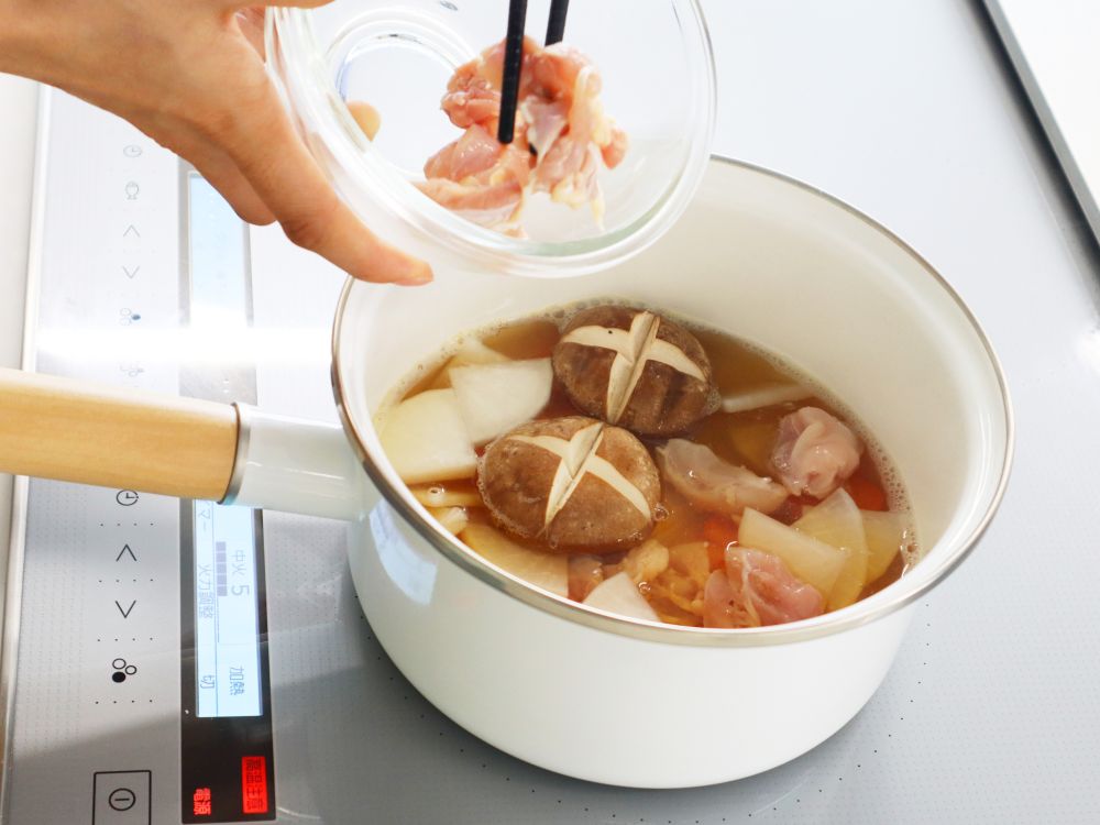 お雑煮の具材を、出汁の入った鍋に入れている写真