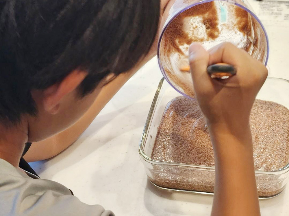 アイチョイスの組合員さんのお子さんである男の子が、お菓子づくりに挑戦している様子の写真。混ぜ合わせた生地を四角い型に流し入れている。