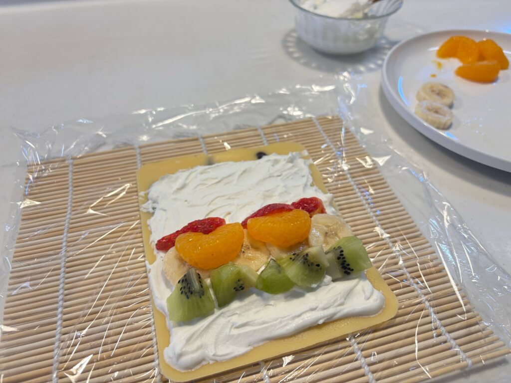 焼きあがった生地に生クリームとフルーツを乗せて巻く