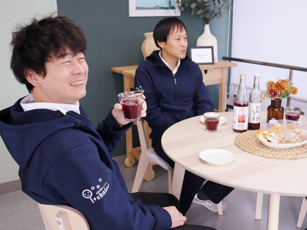 男性職員が食卓でジュースを手にとって微笑んでいる様子