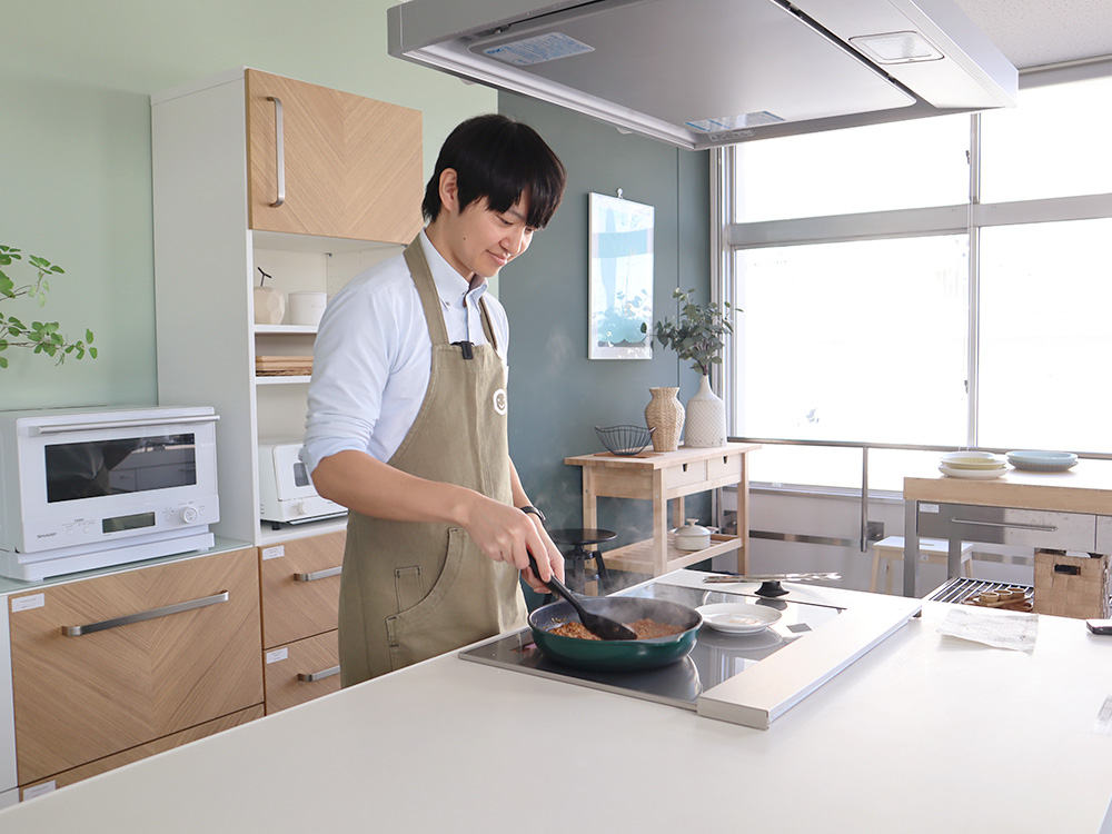 キッチンでフライパンを操りながら調理をしている男性職員Kさん