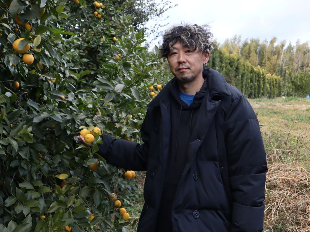 木に実ったレモンに手を添えてほほ笑む伊藤農園の伊藤さん