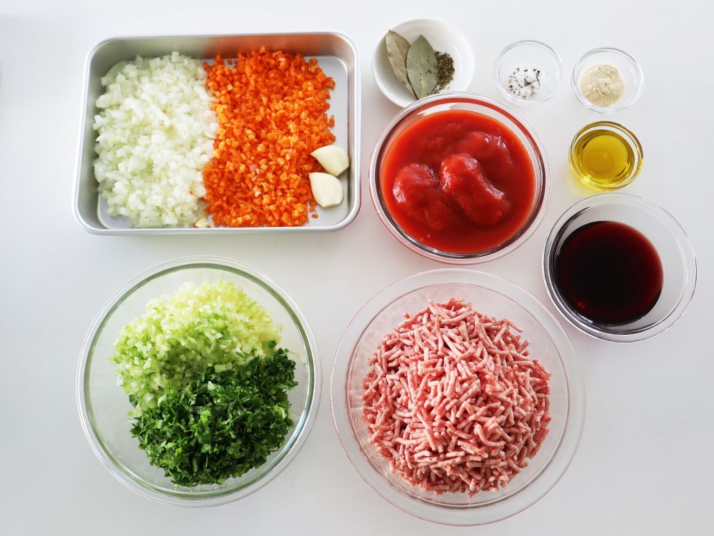 レシピに必要な具材の集合写真 玉ねぎ にんじん にんにく セロリ ひき肉 トマト缶 調味料 香辛料