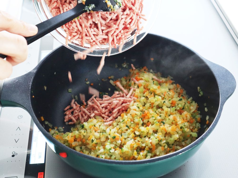 フライパンで炒めた野菜にひき肉を加えているところ