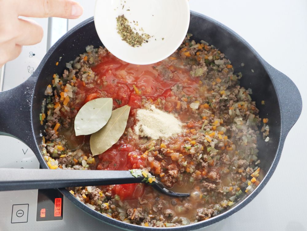 フライパンの調理中の具材にローリエ オレガノ チキンコンソメを加えているところ