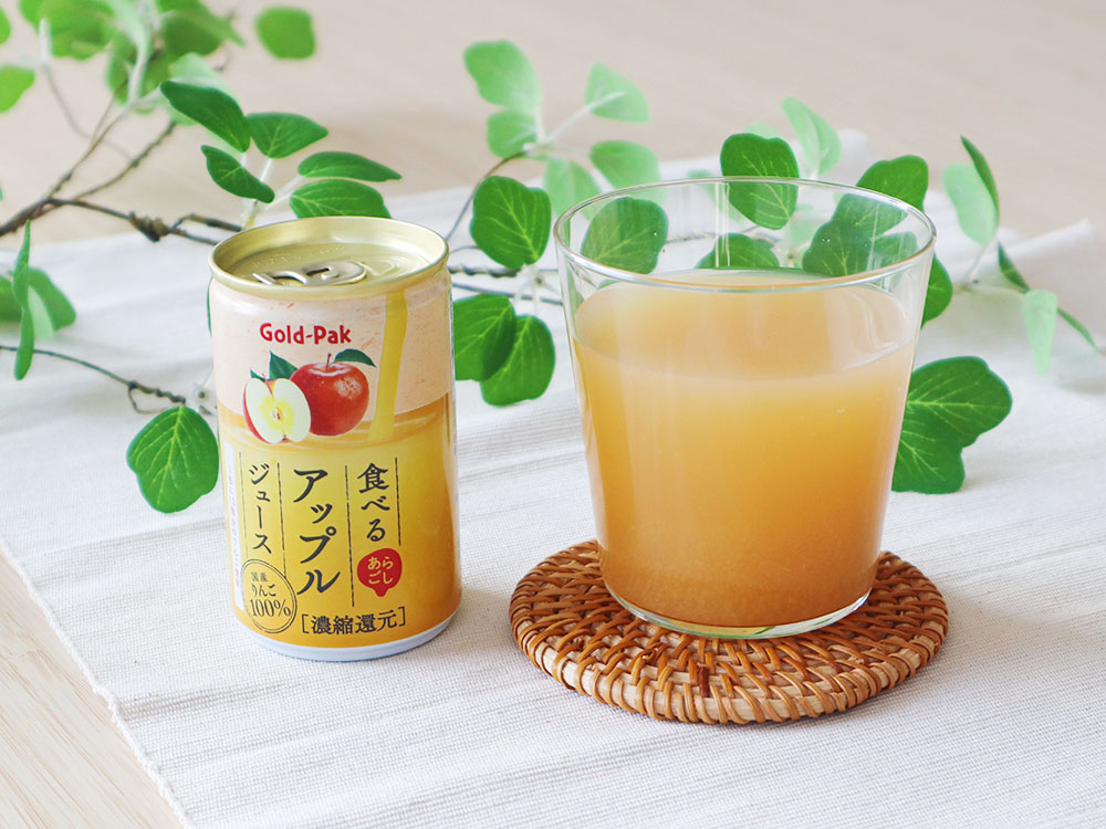 ゴールドパックの商品である『食べるアップルジュース』をコップに注ぎ、パッケージである缶と一緒に並べた写真。