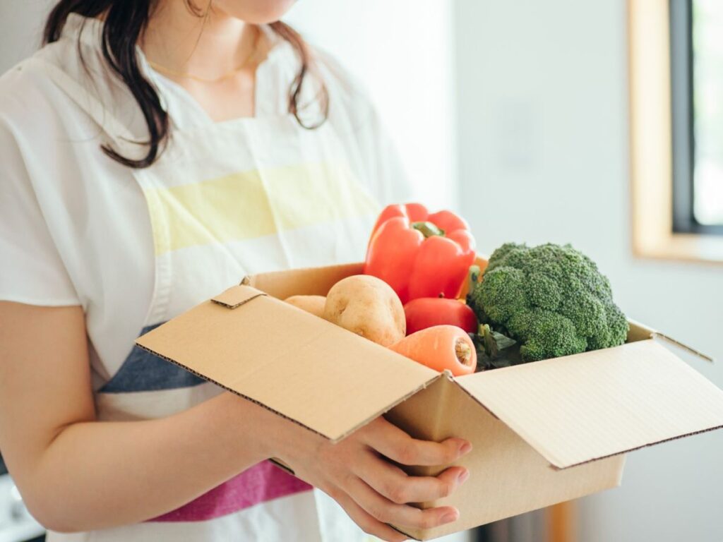 段ボールに入った野菜を持つ女性