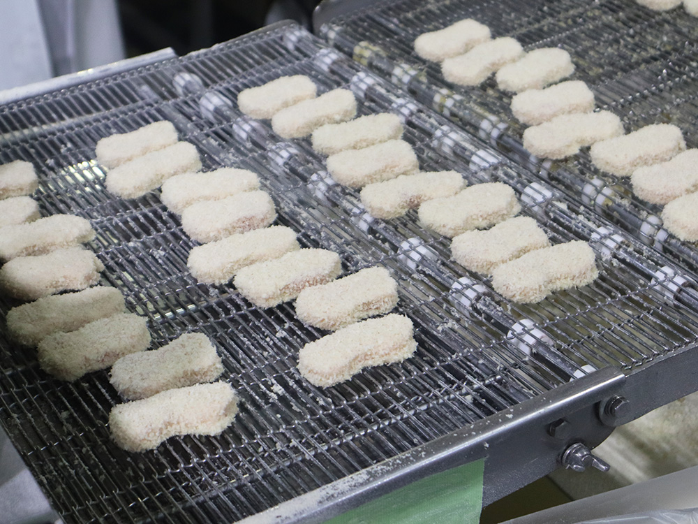微粉パン粉がつき、綺麗に整列され流れていくチキンナゲットの写真