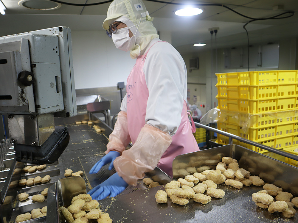 ピンクのエプロンを来た作業員がチキンナゲットの検品をしている写真
