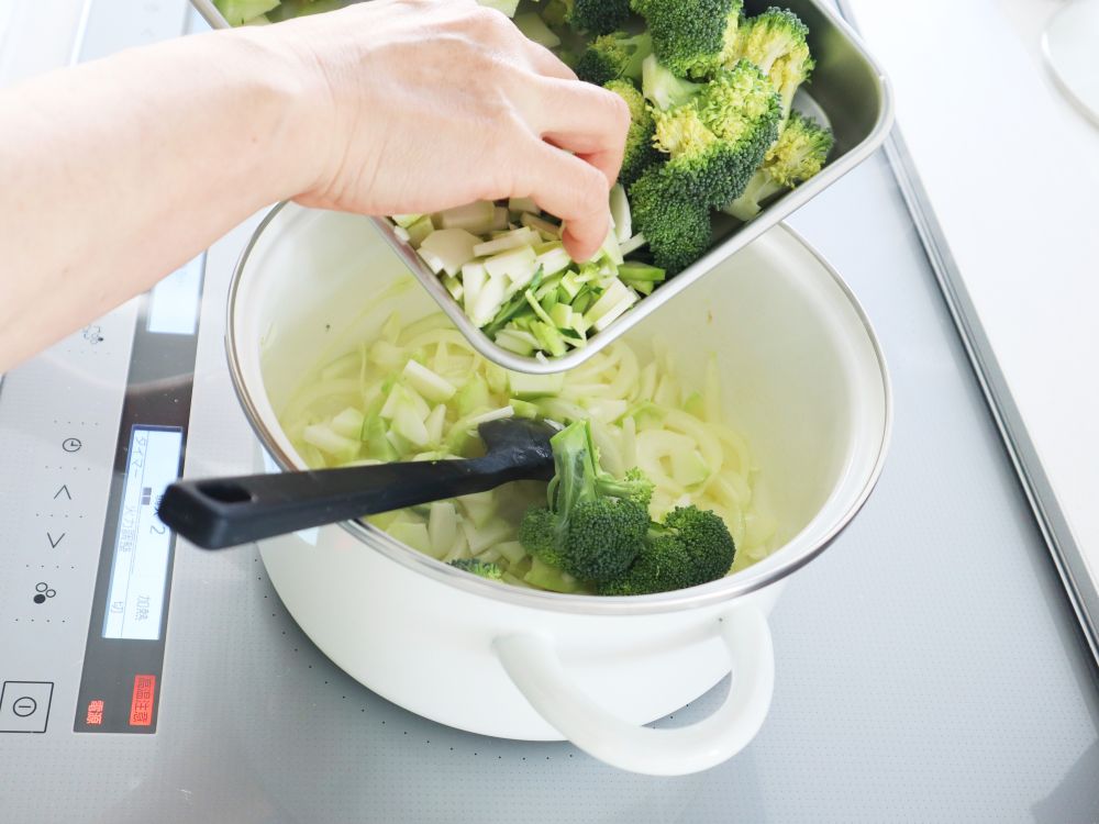 玉ねぎを炒めた鍋に、小房に切ったブロッコリーを入れている様子