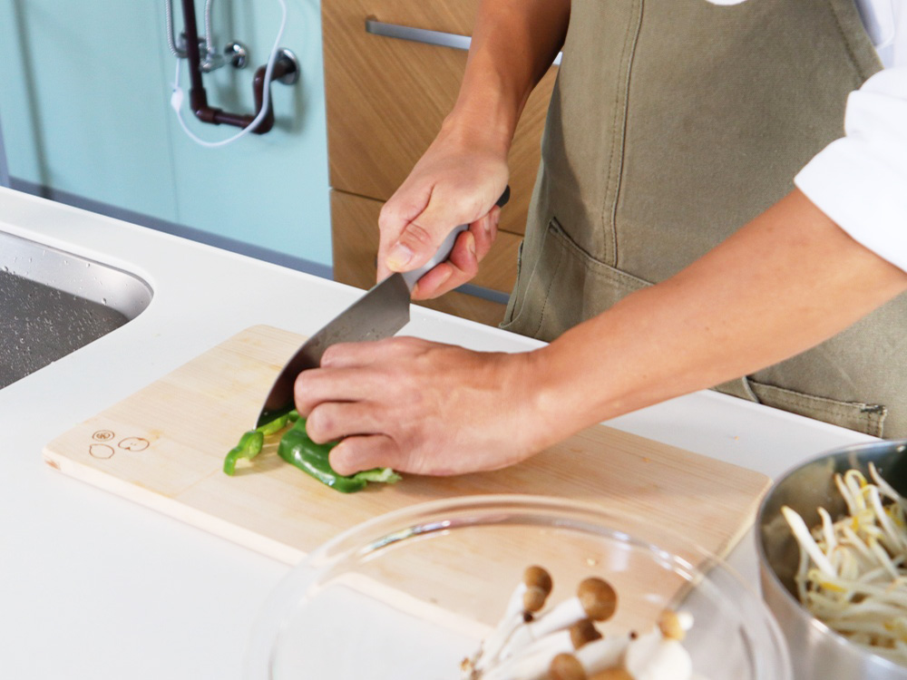 まな板の上で包丁を使って具材を刻む男性職員の手元の写真