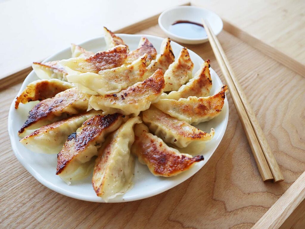 タレとお箸が添えられた大盛りの餃子の写真