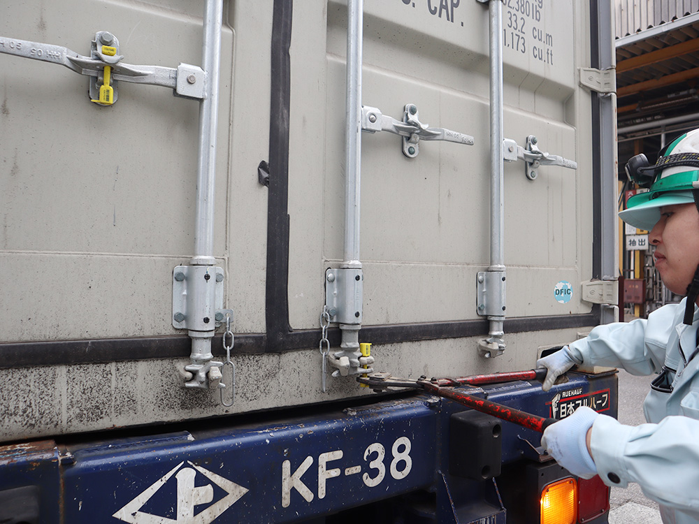 平田産業の敷地内に届いたコンテナの封を、大きなペンチで開けている様子
