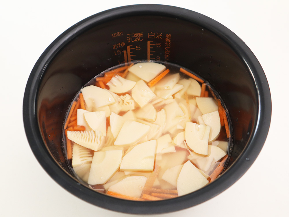 炊飯器に米と調味料と筍やにんじんがセットされている写真