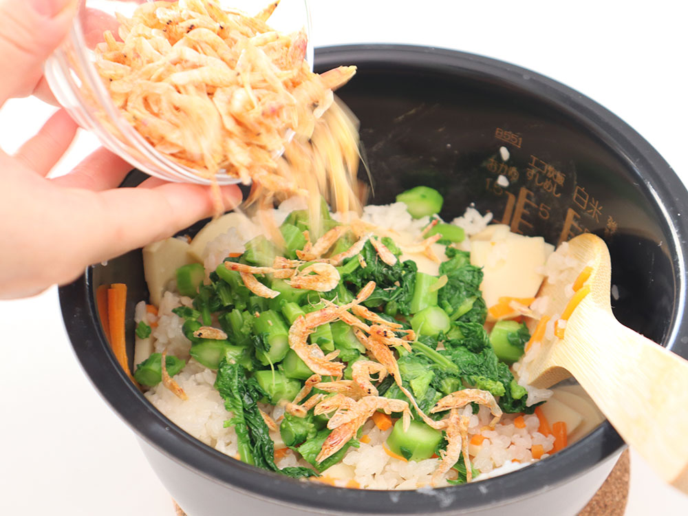 炊飯器で炊きあがった調味ご飯に菜花と桜えびを混ぜ込むシーン