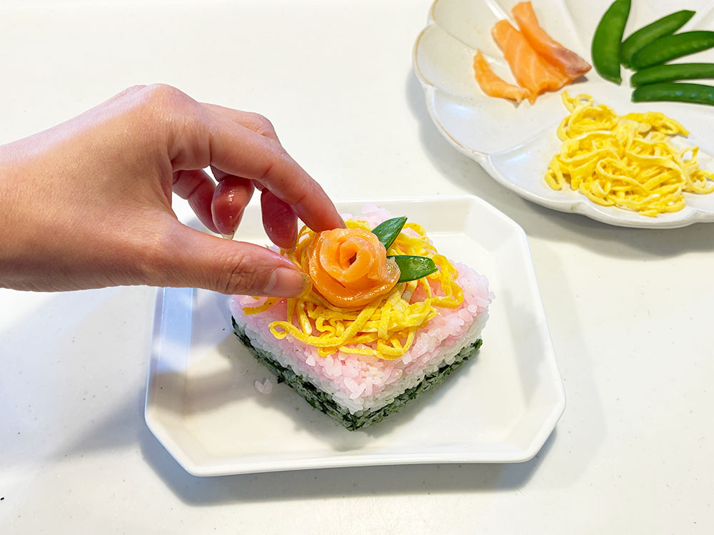 牛乳パックで作ったちらし寿司の仕上げとしてバラに見立てたサーモンを飾りつけているところ
