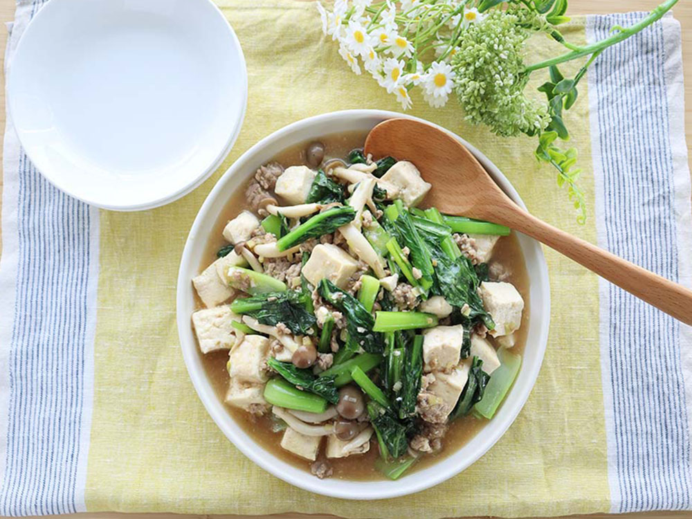 小皿や花などが飾られた小松菜マーボー豆腐の完成品を上から撮影した写真