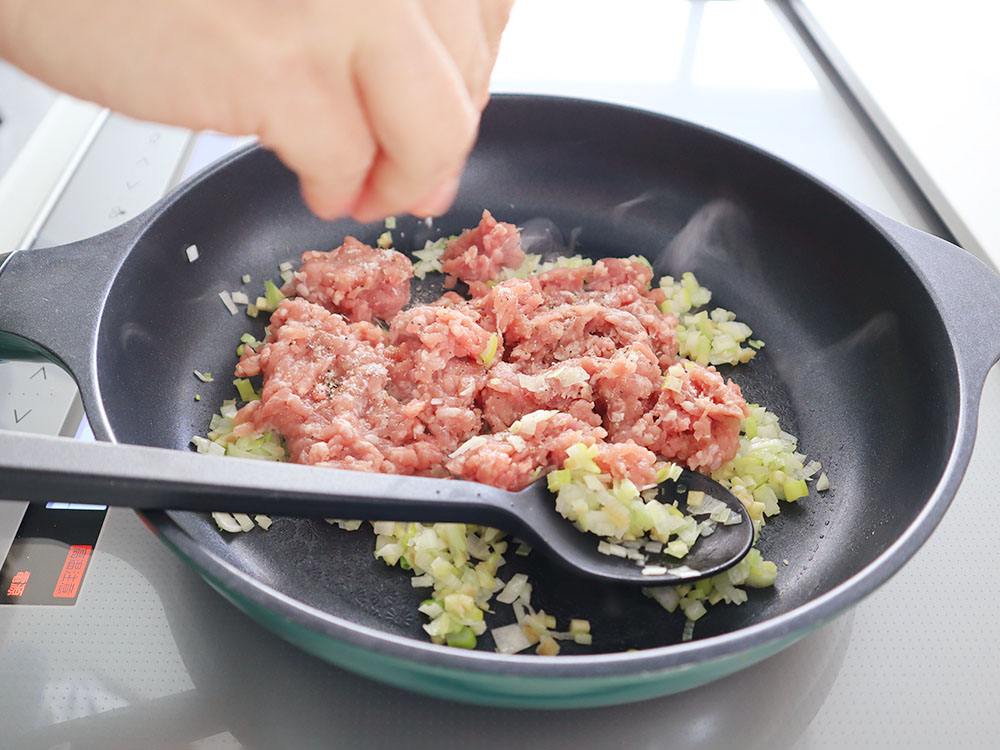 小松菜のマーボー豆腐の調理工程でひき肉や薬味を炒め合わせ塩を振っているシーン