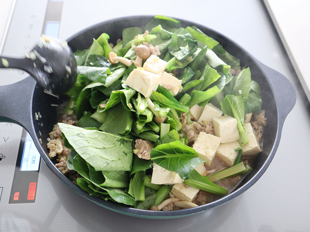 小松菜のマーボー豆腐の調理工程でフライパン上で小松菜や豆腐を炒め合わせているシーン