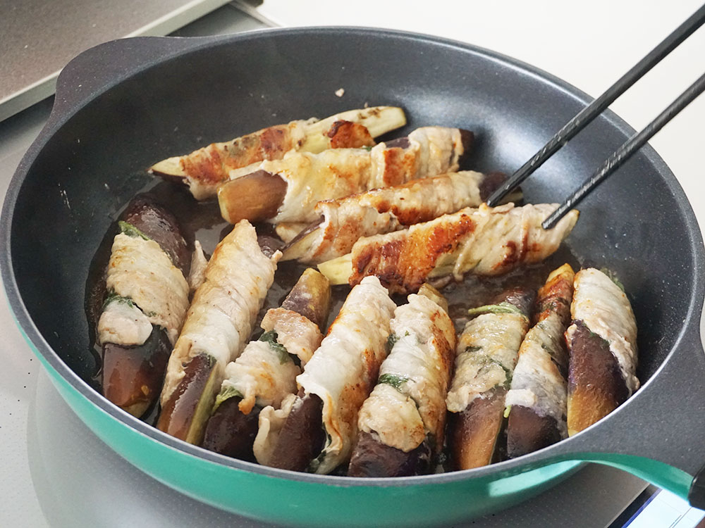 焼けた肉巻きなすに調味料を加えてフライパンで仕上げをする様子